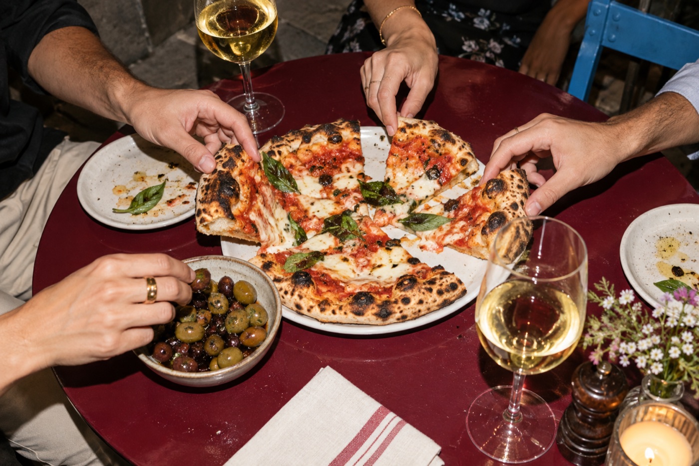 Hände teilen Pizza und Oliven an einem Tisch mit zwei Weingläsern